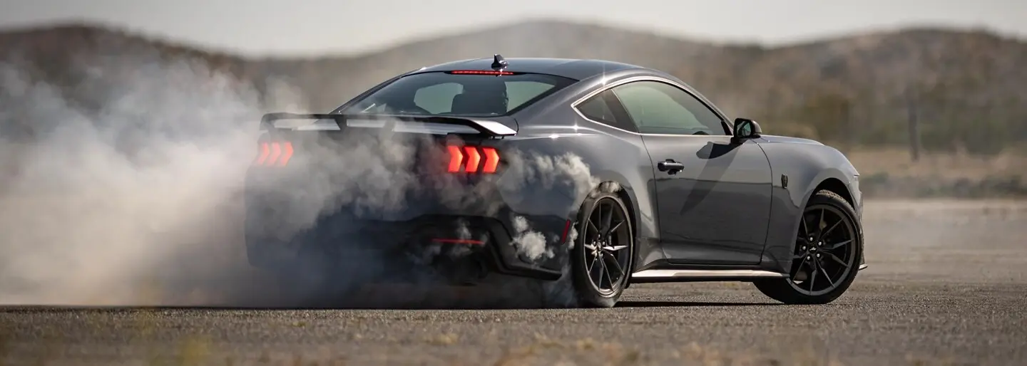 
A dark gray Ford Mustang sports car is drifting on an asphalt road 
