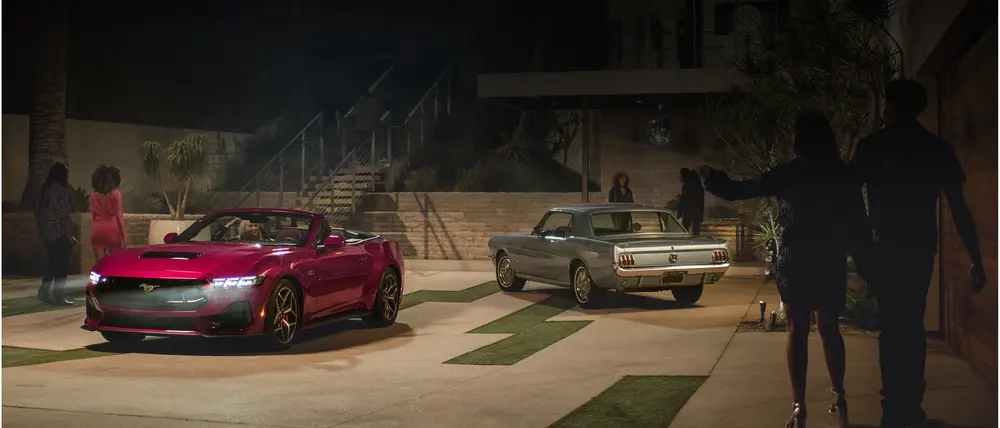 
A pink convertible 2025 Ford Mustang is parked in a modern driveway at night