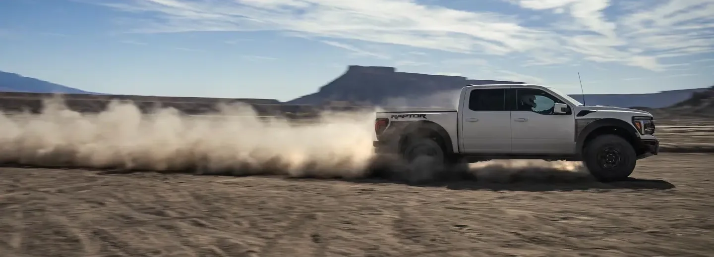 2025 Ford F-150® Raptor R™ pickup in Carbonized Gray being driven in the desert kicking up a cloud of dust