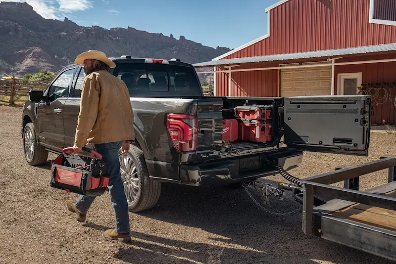 A man walking away from his parked 2025 Ford F-150® carrying his bag of tools, and a trailed attached