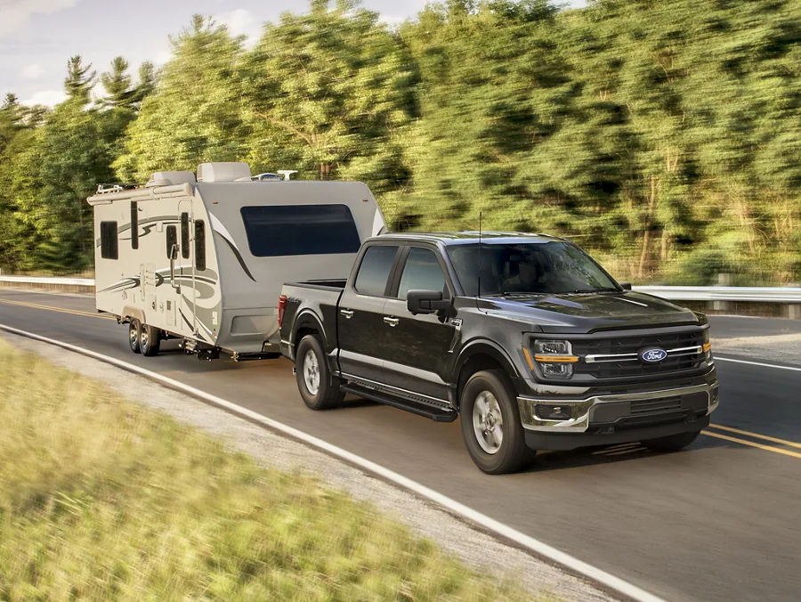 A dark Ford F-150 truck towing a camper trailer on a highway.