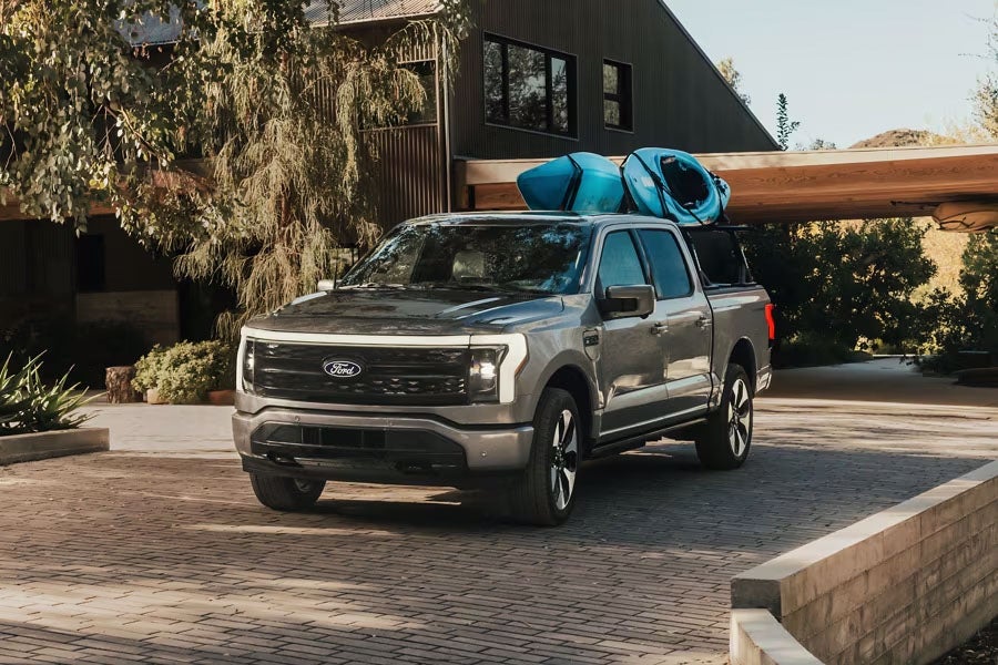 A Ford F-150 Lightning parked in a driveway with kayaks in the pickup bed