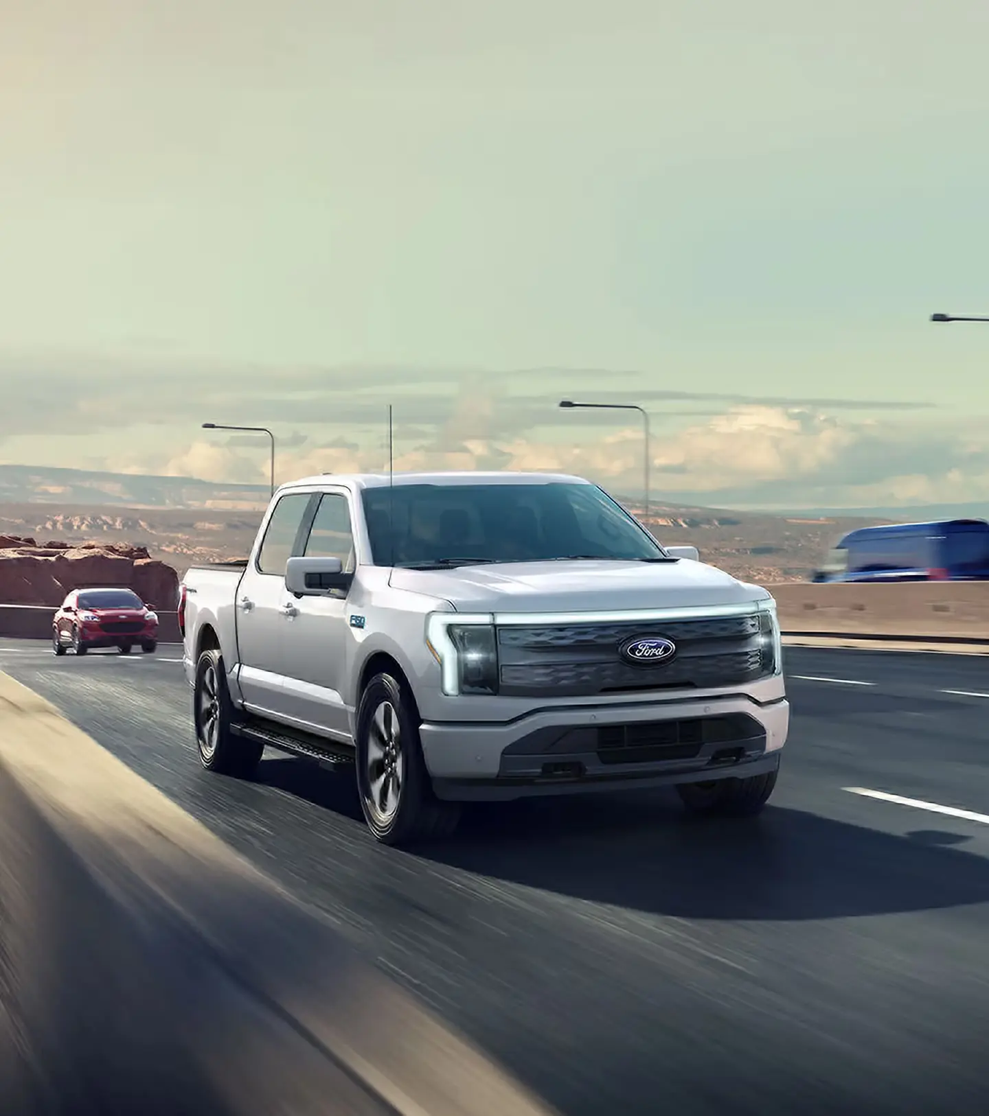 A white Ford F-150 Lightning electric pickup truck driving on a highway on a sunny day.